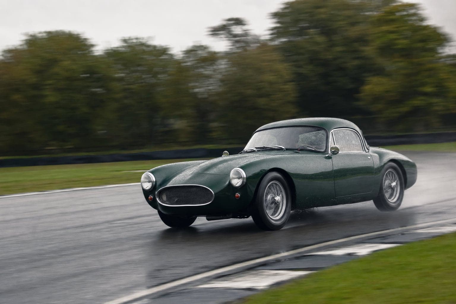 Dark green classic sports car cornering on a wet race circuit